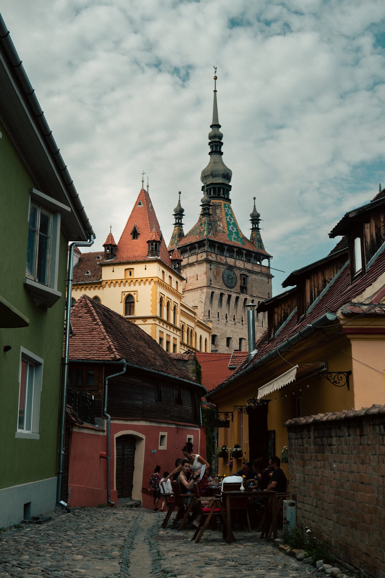 A cobbled street below the clock tower, café tables in the evening light