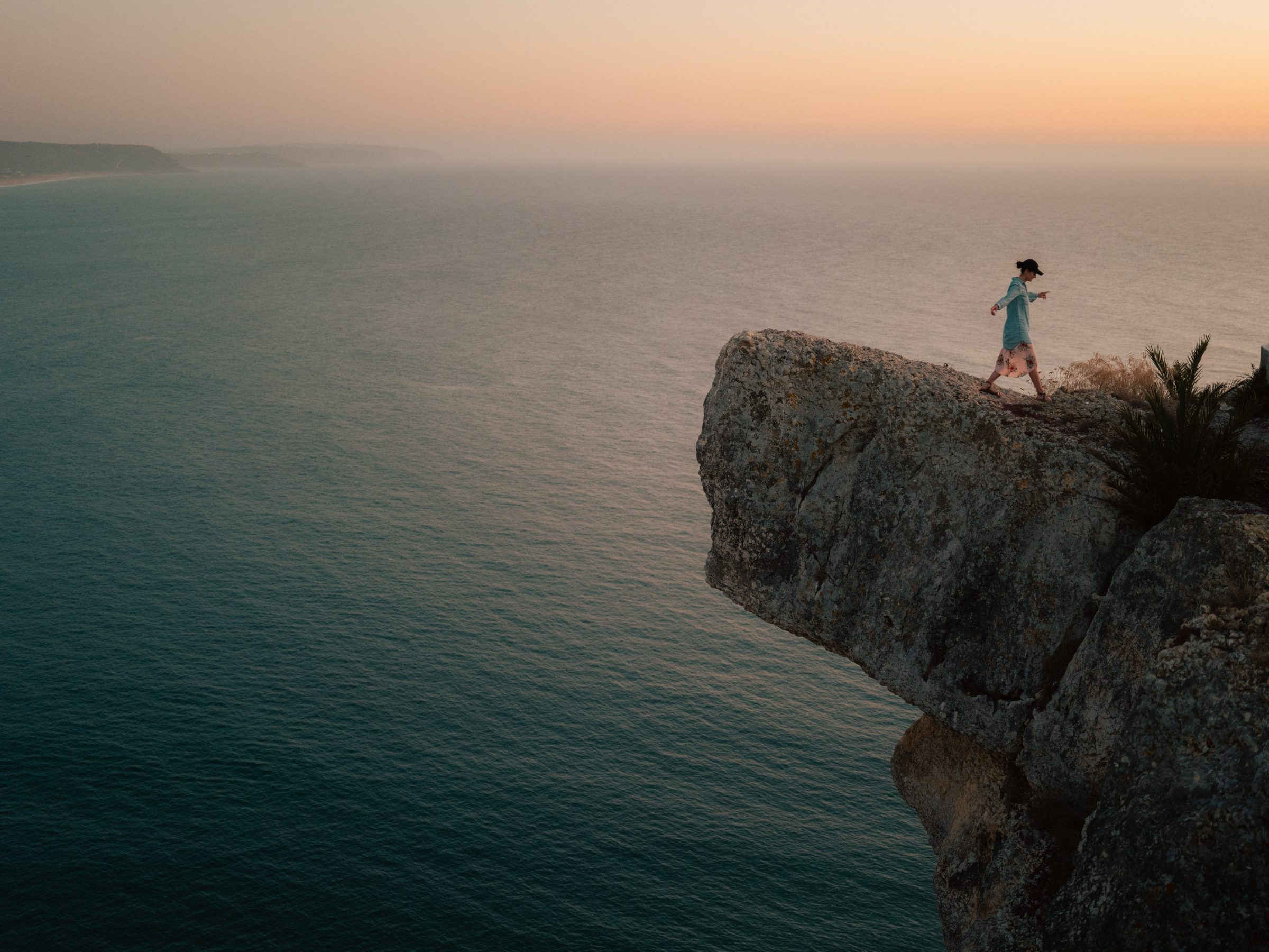A figure walking a cliff edge above the ocean at dusk