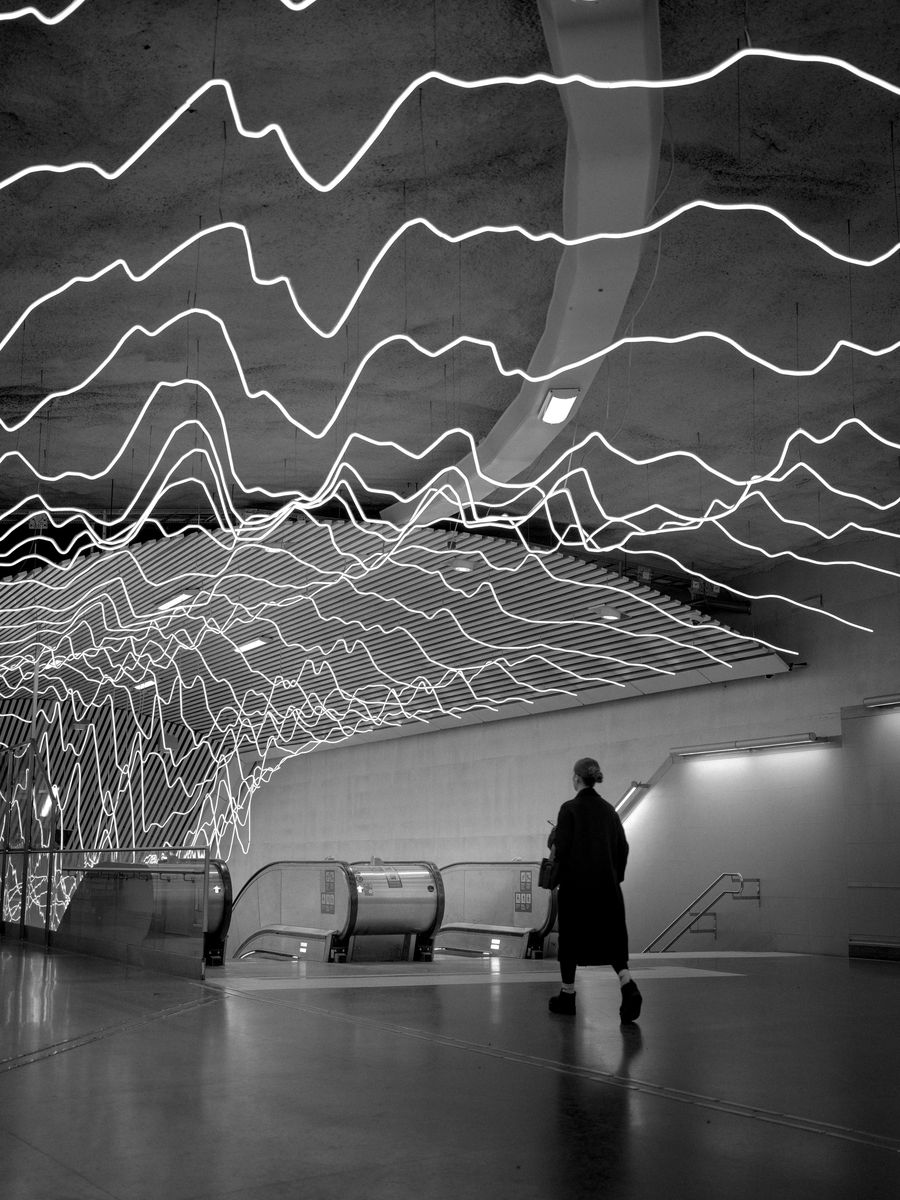 A figure in a subway hall lit by luminous waveforms