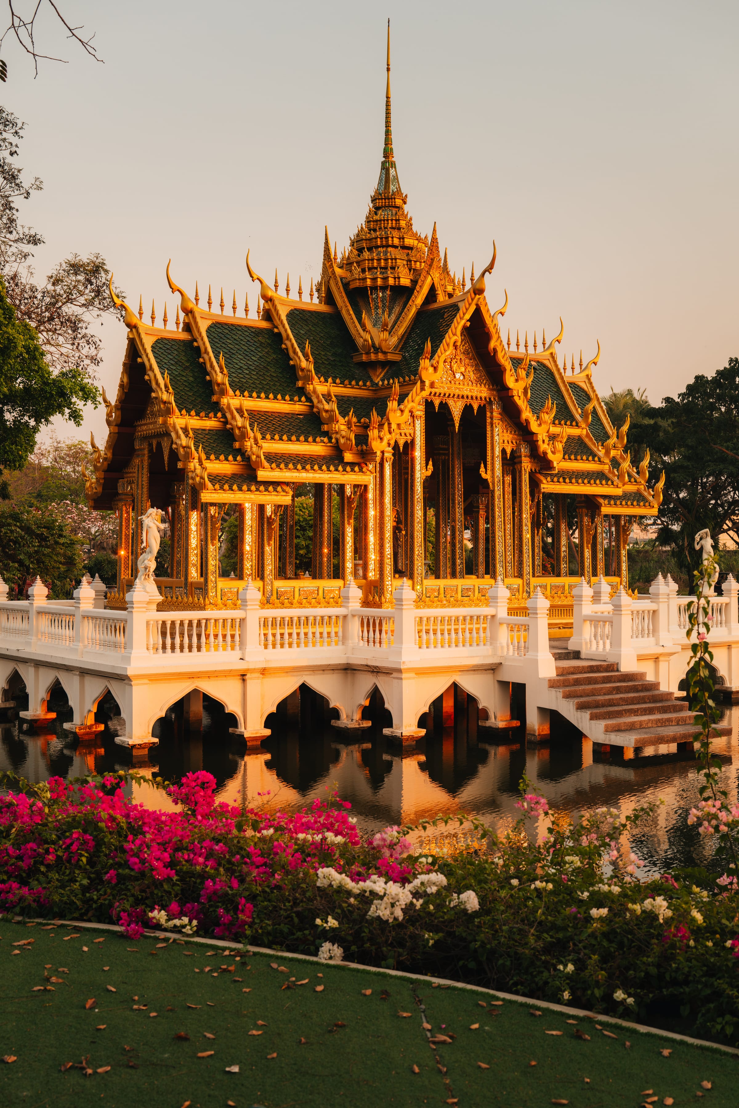 A gilded multi-tiered Thai pavilion mirrored in a still moat, bougainvillea in the foreground.