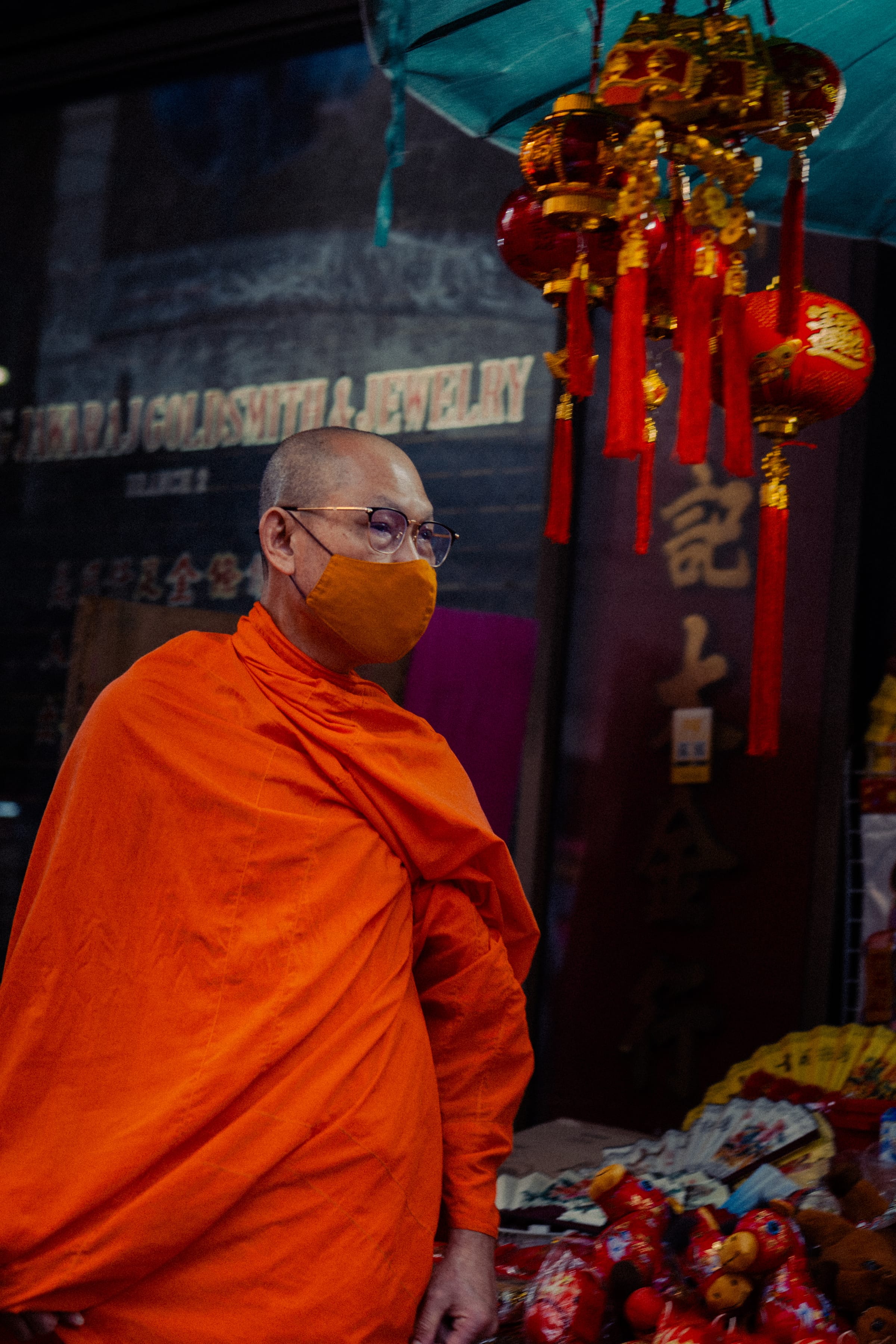 A monk in an orange face mask among red-and-gold Chinatown decorations.