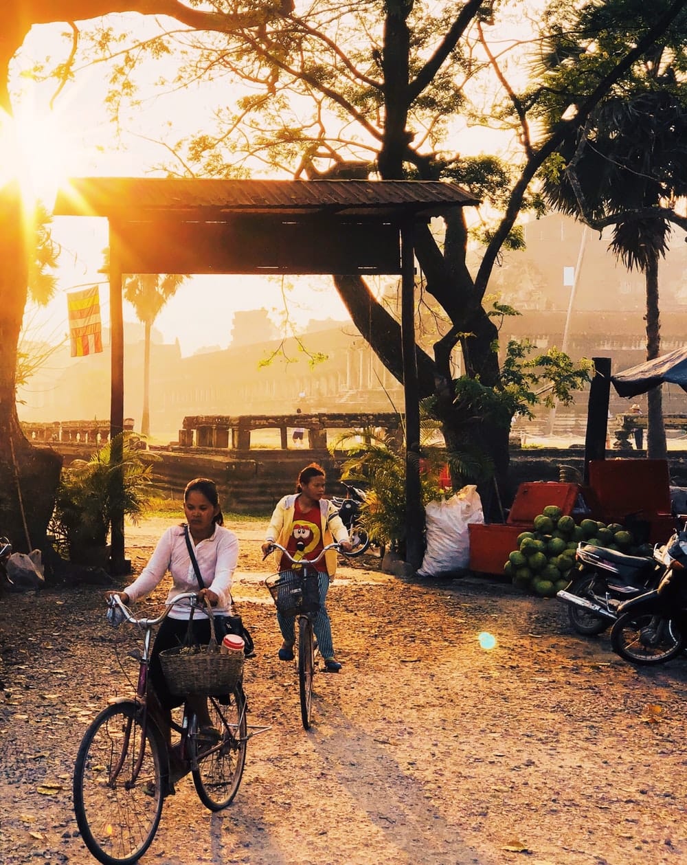 Two women cycling past a food cart at sunrise