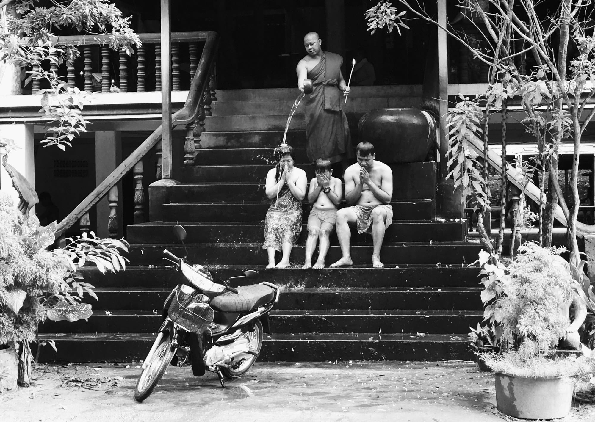 A monk pouring a water blessing over a family on temple steps