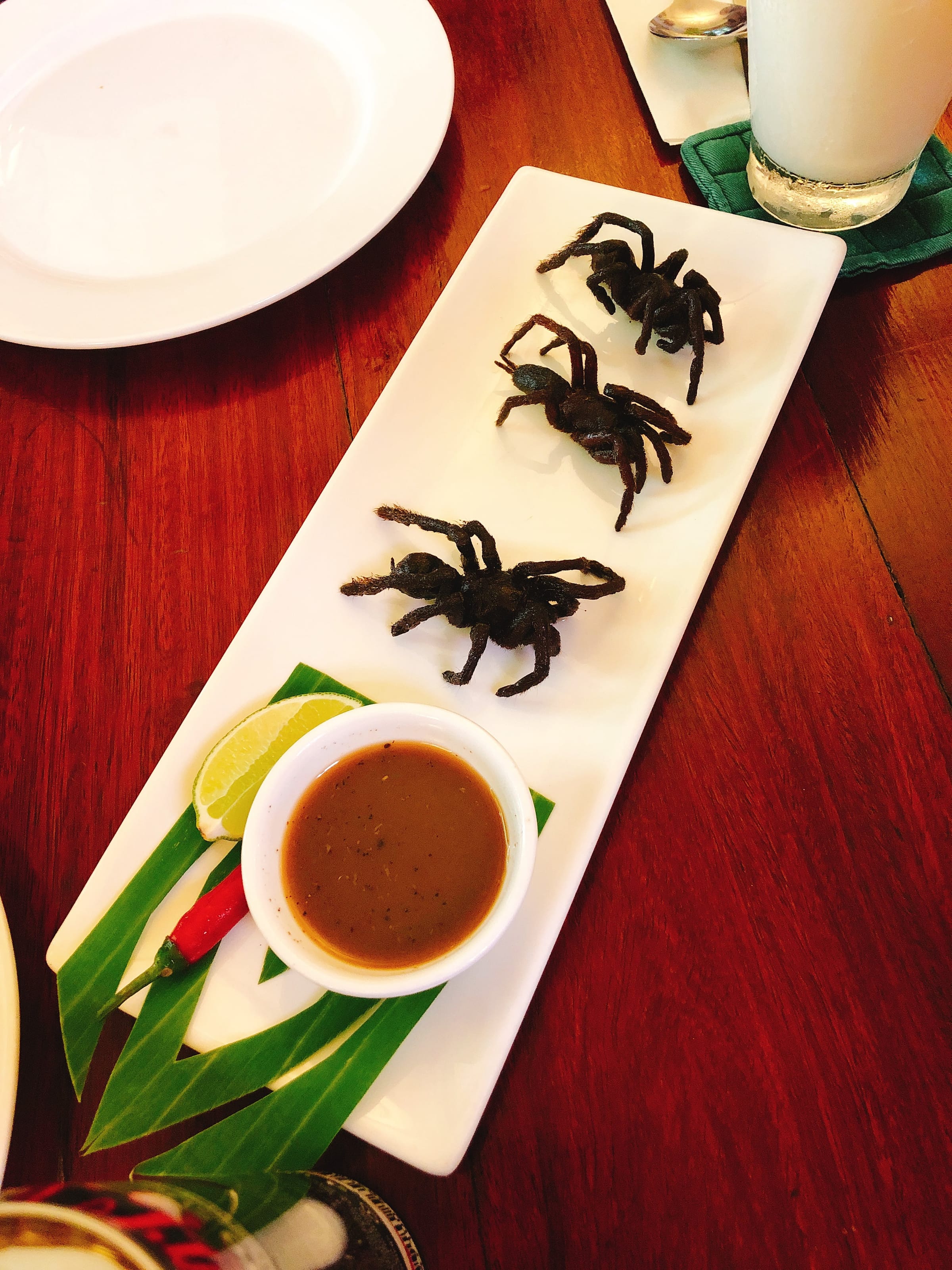 Three fried tarantulas on a plate with lime and dipping sauce